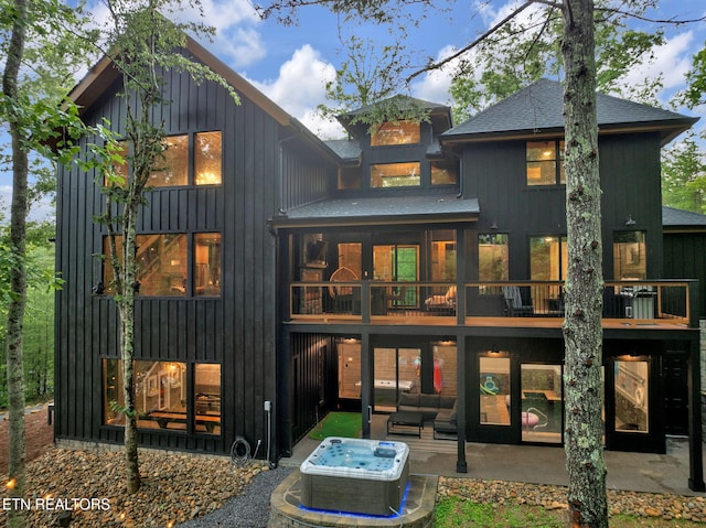 back of property with board and batten siding, a hot tub, a patio, and an outdoor living space