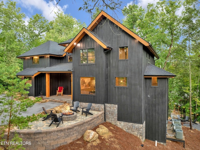 back of property featuring roof with shingles, a patio, and a fire pit