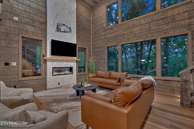 living room featuring a towering ceiling, light wood finished floors, wooden walls, and a premium fireplace