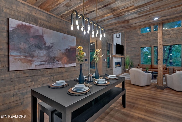 dining room featuring wooden ceiling, a lit fireplace, wood finished floors, and wood walls