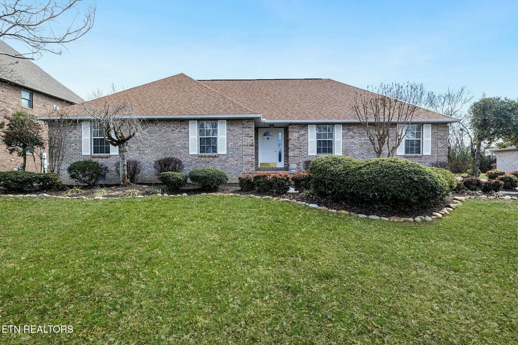 ranch-style home featuring a front lawn, roof with shingles, and brick siding