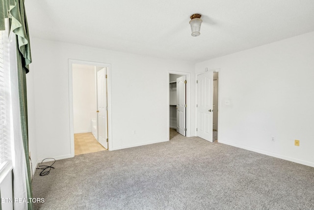 unfurnished bedroom with baseboards, a spacious closet, ensuite bath, and light colored carpet