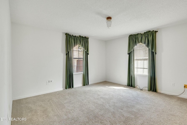 spare room with baseboards, a textured ceiling, and light colored carpet