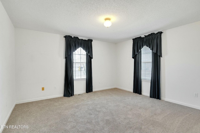 spare room featuring visible vents, light carpet, a textured ceiling, and baseboards