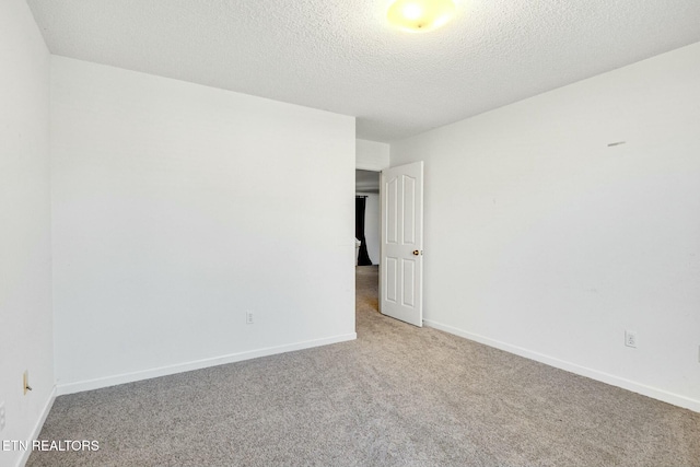 carpeted empty room featuring a textured ceiling and baseboards