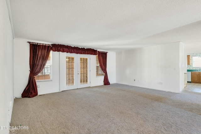 unfurnished room with light colored carpet, a textured ceiling, and french doors