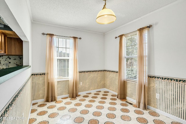 empty room featuring a wainscoted wall, a textured ceiling, and crown molding