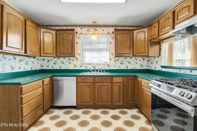 kitchen with appliances with stainless steel finishes, dark countertops, a sink, and wallpapered walls