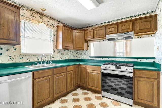 kitchen featuring stainless steel appliances, dark countertops, a sink, under cabinet range hood, and wallpapered walls