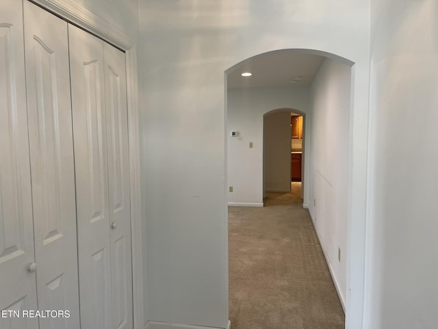 hallway featuring baseboards, arched walkways, and light carpet