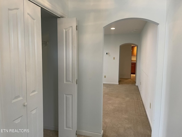 hall featuring baseboards, arched walkways, and light carpet