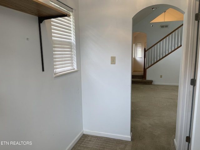 hall with visible vents, arched walkways, carpet, and baseboards