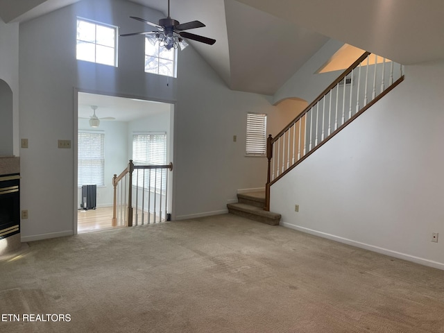 unfurnished living room featuring a ceiling fan, radiator heating unit, carpet floors, baseboards, and a towering ceiling