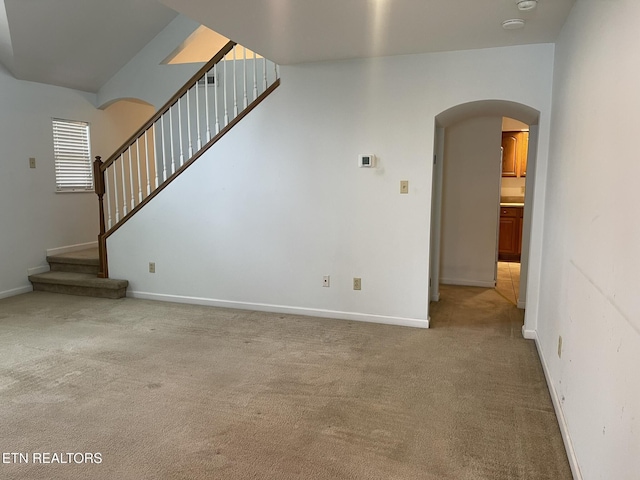 unfurnished living room featuring baseboards, stairway, arched walkways, and light carpet