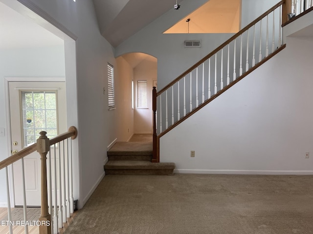 staircase with visible vents, baseboards, carpet floors, a high ceiling, and arched walkways