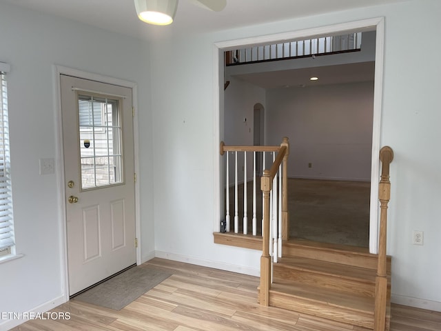 foyer with arched walkways, baseboards, and light wood-style floors