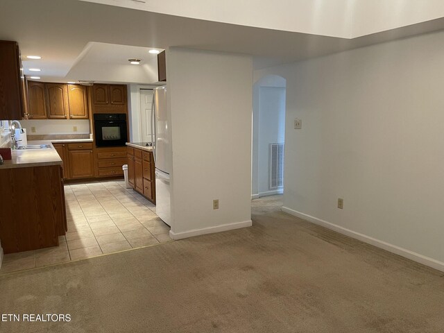 kitchen featuring oven, a sink, arched walkways, baseboards, and light colored carpet