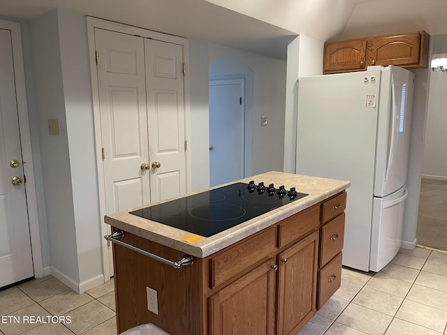 kitchen featuring light tile patterned floors, freestanding refrigerator, light countertops, black electric cooktop, and a center island