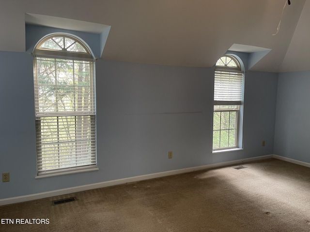 carpeted empty room featuring vaulted ceiling, baseboards, and visible vents