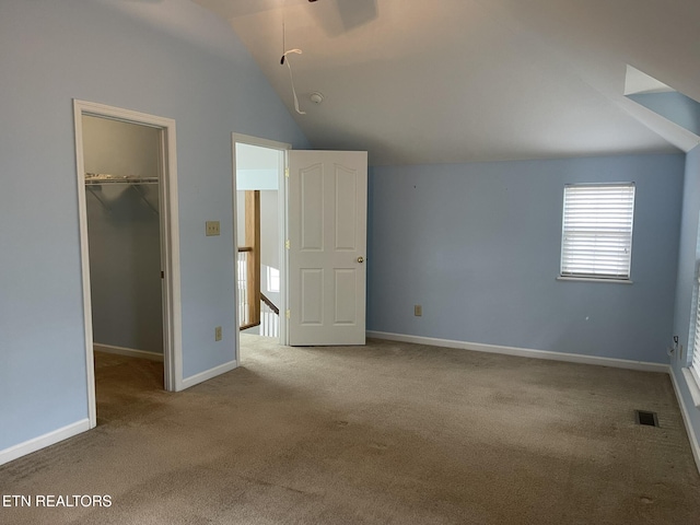 unfurnished bedroom featuring a spacious closet, visible vents, baseboards, lofted ceiling, and carpet floors