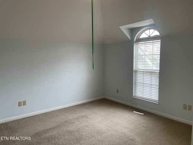 spare room featuring vaulted ceiling, carpet, and baseboards