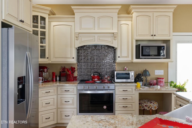 kitchen featuring custom range hood, stainless steel appliances, cream cabinets, and light stone counters