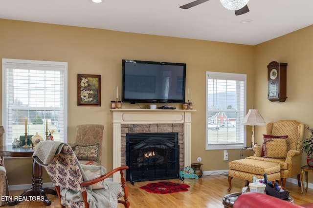 living room with ceiling fan, wood-type flooring, and a stone fireplace