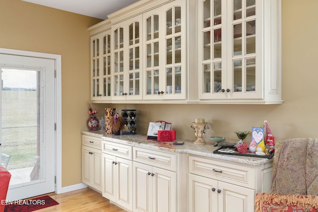 kitchen featuring cream cabinets, light wood-type flooring, and light stone countertops