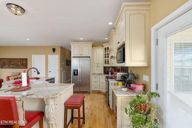 kitchen featuring appliances with stainless steel finishes, light stone counters, cream cabinets, a breakfast bar, and sink