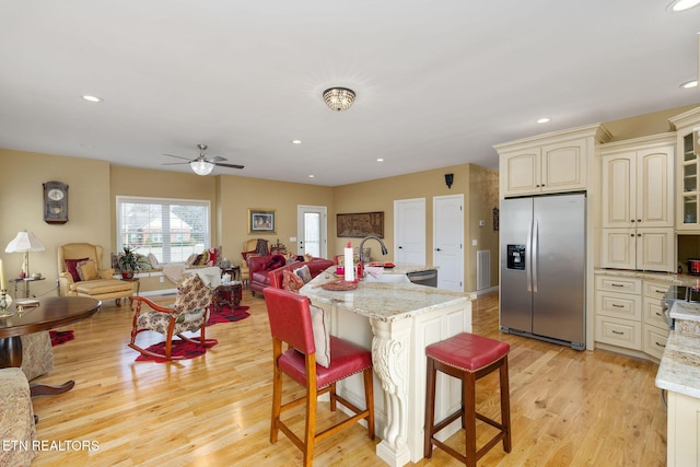 kitchen with light hardwood / wood-style flooring, stainless steel refrigerator with ice dispenser, cream cabinetry, light stone countertops, and a breakfast bar area