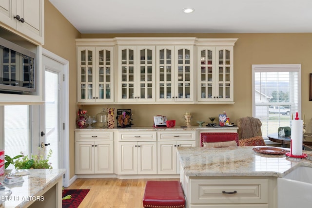 kitchen with light wood-type flooring, cream cabinets, and light stone countertops