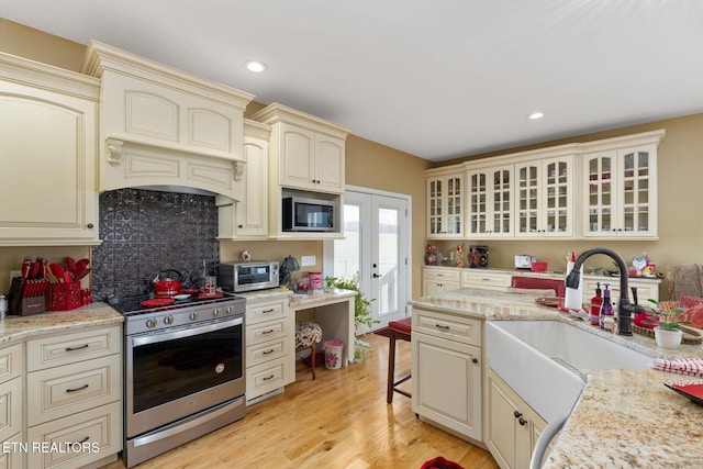 kitchen with sink, light hardwood / wood-style floors, stainless steel appliances, light stone countertops, and cream cabinets