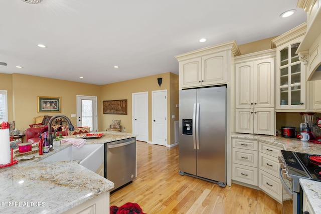 kitchen with light stone countertops, sink, stainless steel appliances, and cream cabinets