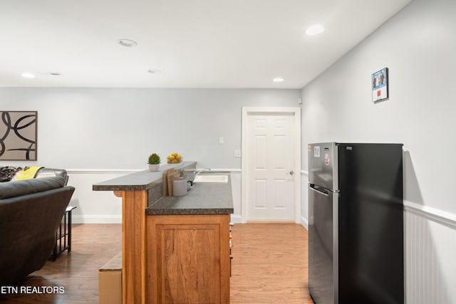 kitchen with light wood-style floors, freestanding refrigerator, a sink, and dark countertops