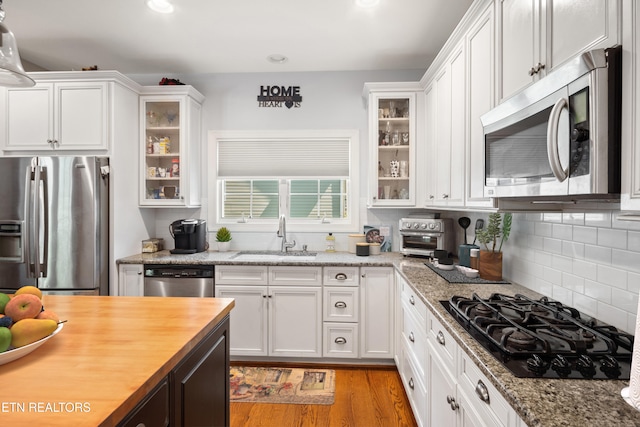 kitchen with stainless steel appliances, decorative backsplash, glass insert cabinets, white cabinetry, and a sink