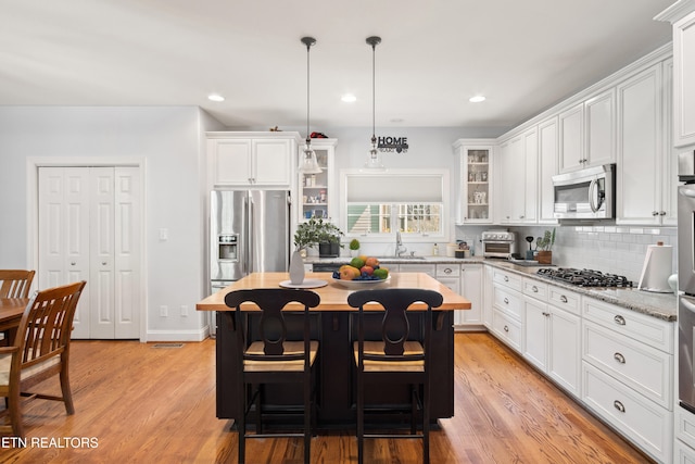 kitchen featuring pendant lighting, stainless steel appliances, light stone counters, and white cabinets