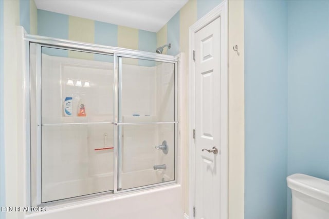 bathroom featuring toilet and shower / bath combination with glass door