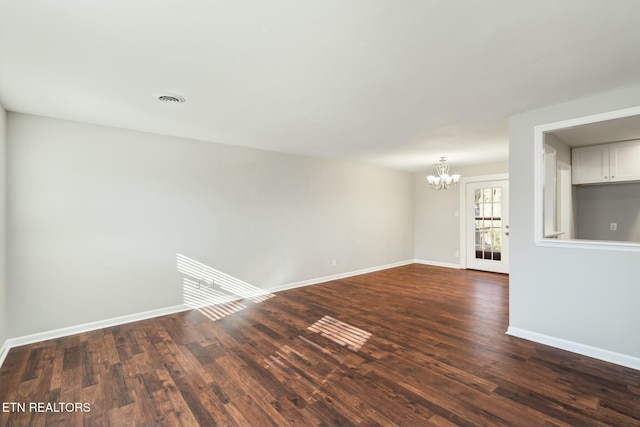 spare room with an inviting chandelier and dark hardwood / wood-style floors