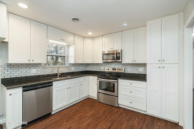 kitchen featuring appliances with stainless steel finishes, sink, dark wood-type flooring, white cabinets, and tasteful backsplash