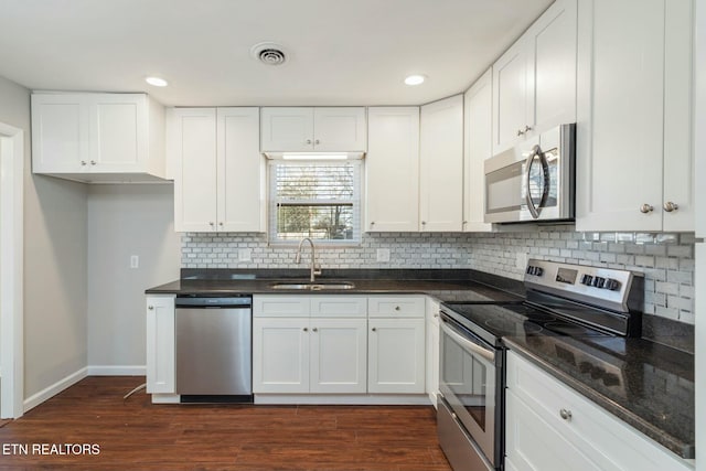 kitchen with appliances with stainless steel finishes, white cabinets, dark hardwood / wood-style flooring, sink, and dark stone countertops