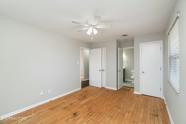 unfurnished bedroom with ensuite bathroom, light hardwood / wood-style floors, ceiling fan, and two closets