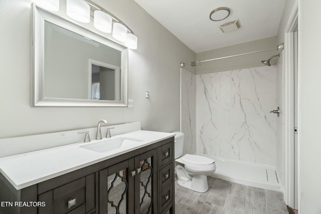 bathroom featuring vanity, a tile shower, and toilet