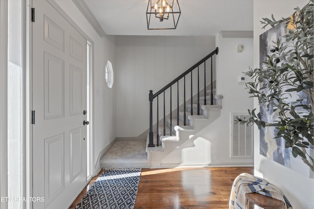 foyer featuring baseboards, visible vents, wood finished floors, stairs, and a notable chandelier