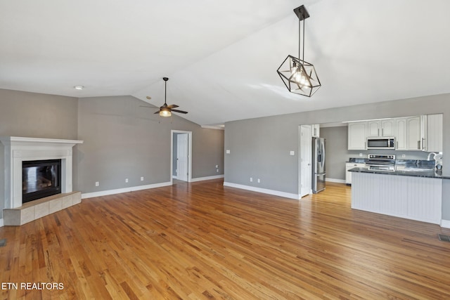 unfurnished living room featuring ceiling fan, light wood-type flooring, vaulted ceiling, and a fireplace
