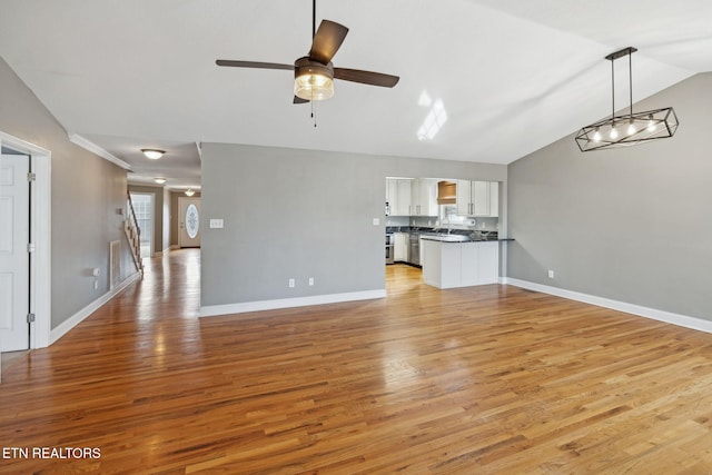 unfurnished living room with vaulted ceiling, ceiling fan, baseboards, and light wood-style floors