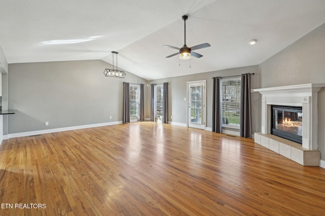 unfurnished living room with light wood finished floors, lofted ceiling, ceiling fan, a tile fireplace, and baseboards