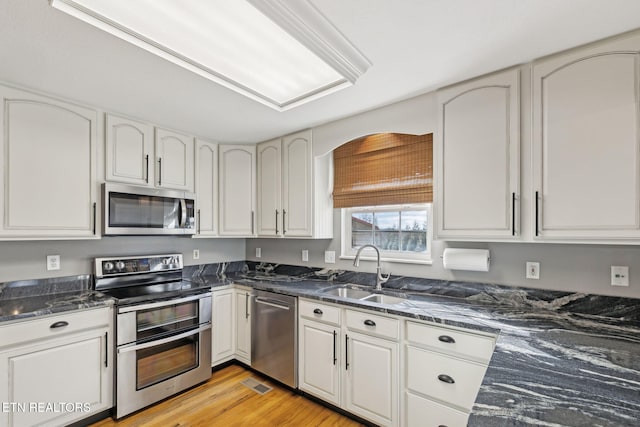 kitchen featuring appliances with stainless steel finishes, light wood-style floors, white cabinetry, and a sink