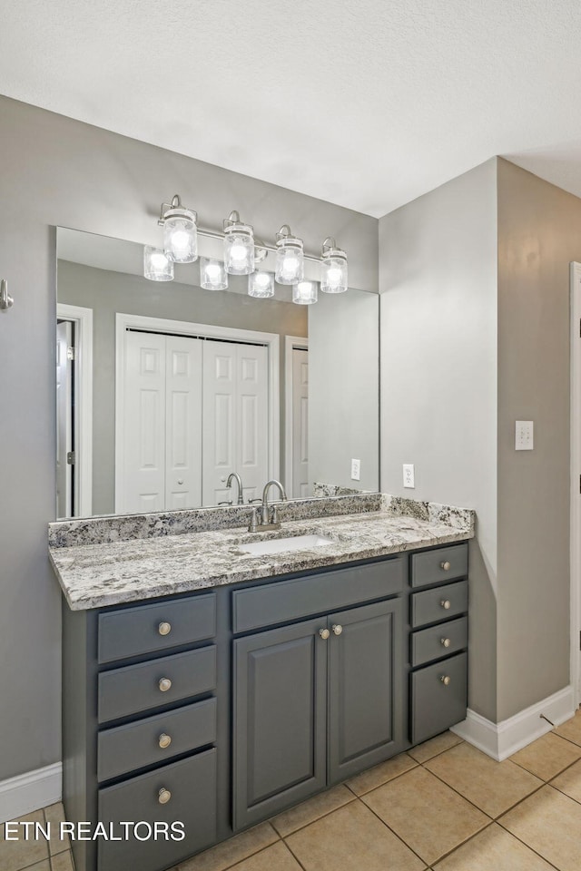 bathroom with a closet, tile patterned flooring, vanity, and baseboards