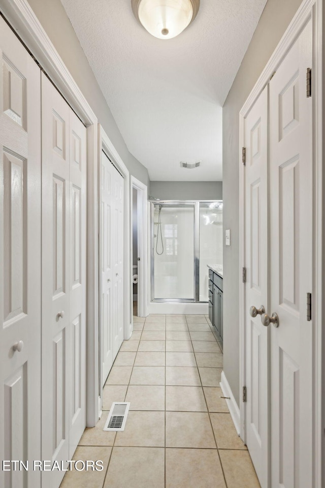 hall featuring visible vents, a textured ceiling, and light tile patterned flooring