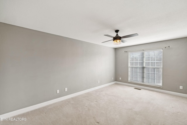 spare room featuring light carpet, visible vents, a ceiling fan, and baseboards